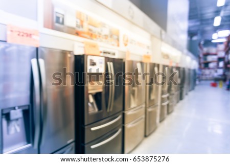 Blurred background retail store with rows of home appliances equipments. Defocused brand new wide selection of French door refrigerators with ice makers. Row of fridges with price tags on display.