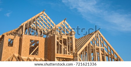 Close-up of gables roof on stick built home under construction and blue sky in Humble, Texas, USA. New build roof with wooden truss, post and beam framework. Timber frame house, real estate. Panorama