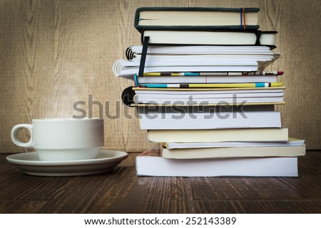 Books stacked and coffee with steam on a wooden table