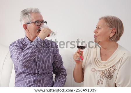 Happy senior couple drinking red wine in their home on a white couch