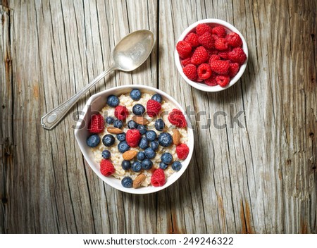 Oatmeal with almonds and berries in a white bowl on wooden background