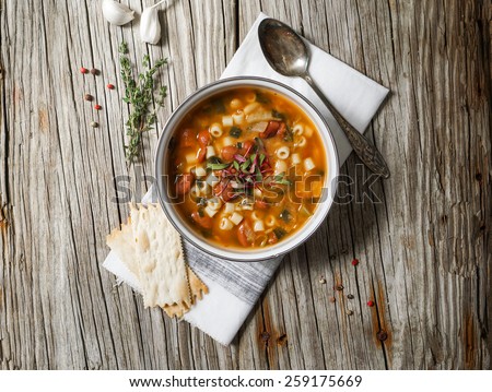A bowl of minestrone soup with crackers on rustic/ vintage background
