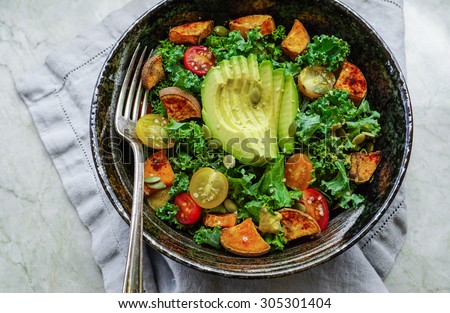 Kale, roasted yams and avocado salad on stone background
