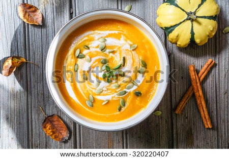 Roasted pumpkin and carrot soup with cream and pumpkin seeds on white wooden background