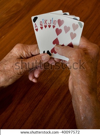 seniors hands holding a winning plaing card hand of a straight flush of hearts