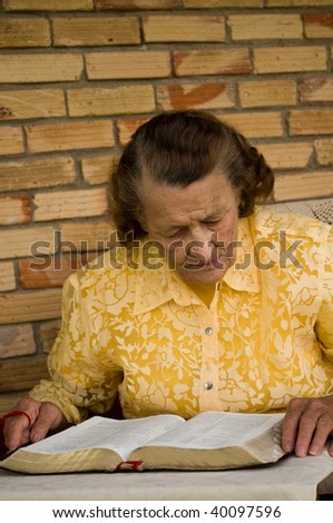 elderly caucasian woman with hands holding Bible as she reads studies the Word