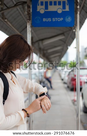 A female(woman) looking at her smart watch, background bus stop.