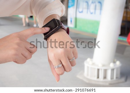A female(woman) hand hold(touch) a smart watch on her left hand.