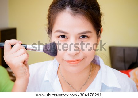 Closeup portrait of a woman applying dry cosmetic tonal on the face using makeup brush.