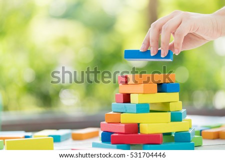 Close-up of asian woman\'s hand playing colorful wood blocks stack game in morning light with copyspace, playing and learning background concept