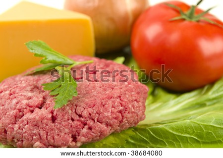 Raw hamburger patty with raw toppings.  Focus on front of hamburger patty.