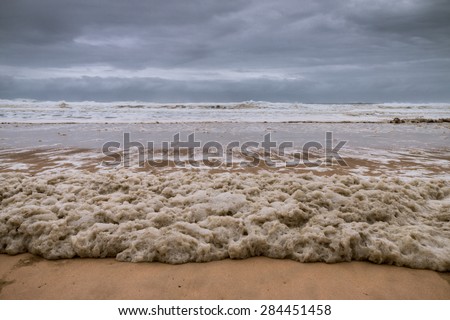 Stormy sea and skies and a beach covered in sea foam