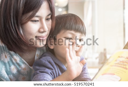 Asian Mother is teaching her son to read a story book