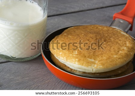 Closeup of pan with pancakes and a glass of milk on the wood background.