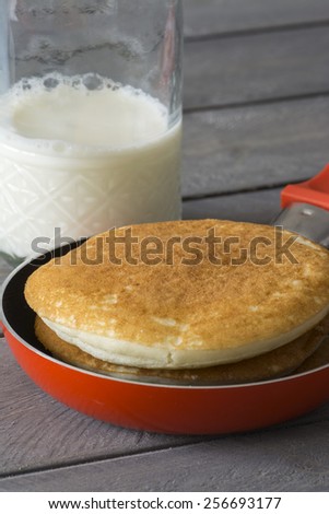 Closeup of pan with pancakes and a glass of milk on the wood background.