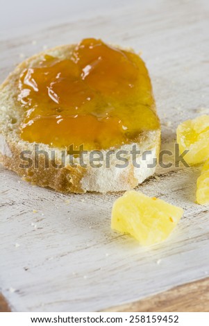 Closeup of  jelly sandwich and a pieces of sugared pineapple on a wood.