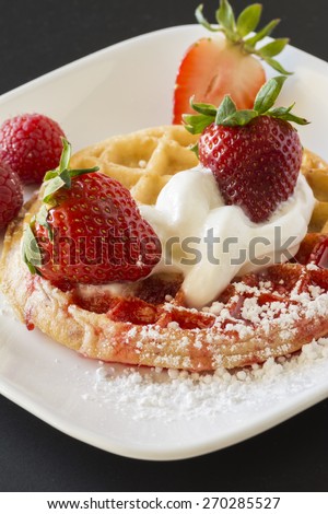 Closeup of waffle and  strawberries with strawberry sauce and whip cream.