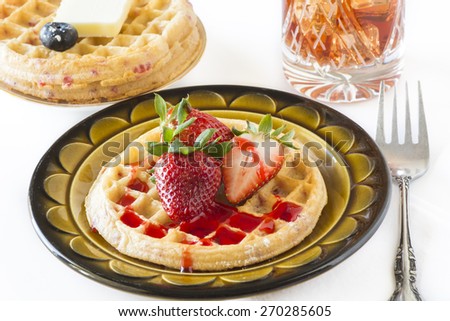 Closeup of waffle and strawberries with strawberry sauce on a white background.