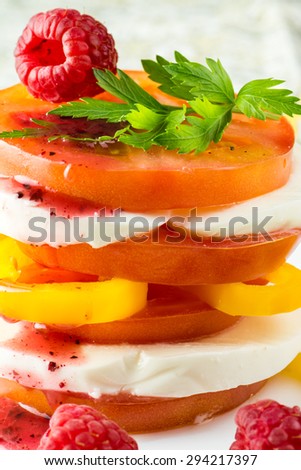 Closeup of tomato stack salad with fresh mozzarella, pepper and raspberry dressing on a white plate.