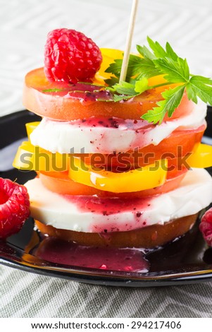Closeup of tomato stack salad with fresh mozzarella, pepper and raspberry dressing on a black plate.