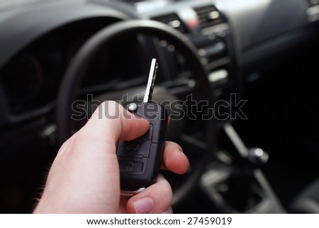 Hand holding a car key an a dar background of a car board