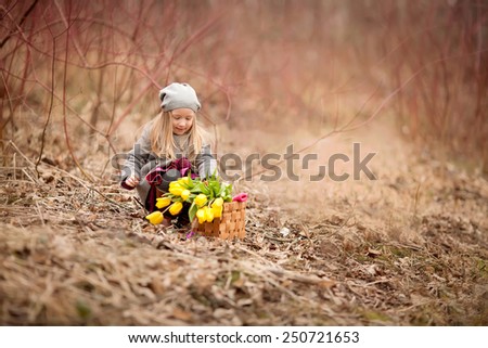 little girl with yellow flowers in the basket sitting in the forest at spring time