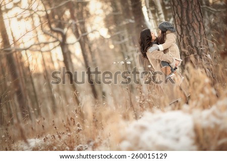 Asian mother holds on hands her little cute daughter in winter forest with tenderness  in the evening when the sun goes down