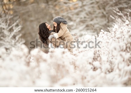 Asian mother with her daughter are standing arm in snowing winter forest and playing and laughing together