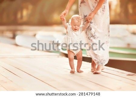 beautiful mother is walking on the pier with her little baby girl daughter with first steps