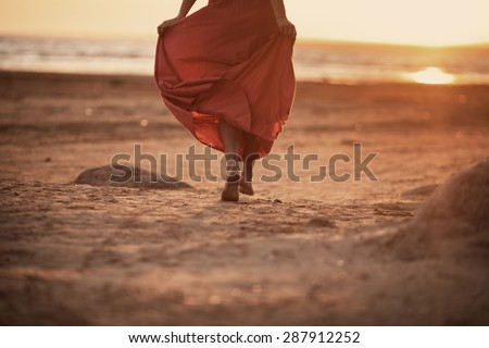 beautiful women in long orange dress is running on the beach at sunset