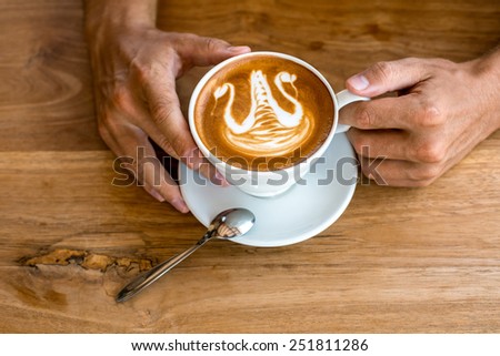 Ceramic white cup of coffee cappuccino on saucer with silver spoon on wooden table in man`s hands