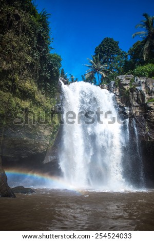 Waterfall and rainbow surrounded with green tropical forest and rocks, vertical