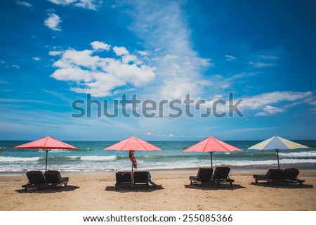 Four sun umbrellas stay on yellow sand beach with blue sea and blue sky on background