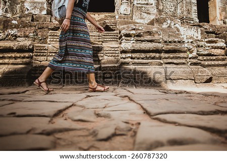 Legs of woman who make a step forward on stone floor with ruins of Angkor Wat on background
