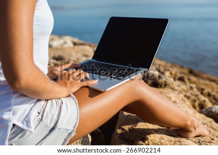 Young woman with slim legs typing on the laptop with blue sea on the background