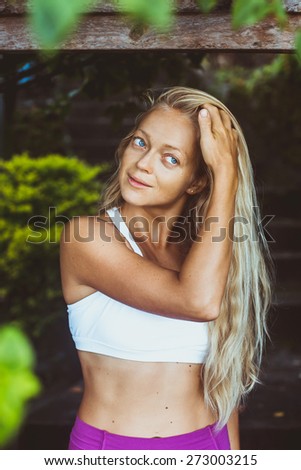 Attractive woman with beautiful long blonde hair and slim body stay in sport wear under the tree, hand in the hair