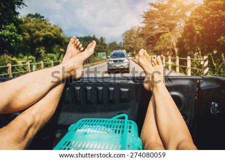 Legs of hitchhiker man and woman traveling in pickup car with the road view on background, vintage style