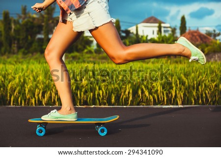 Girl skateboarder legs skateboarding at sunset rice fields