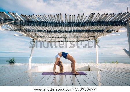 Woman with long hair and slim body make morning yoga exercise on the yoga mat on white wooden terrace. Yoga pose. Bridge pose.