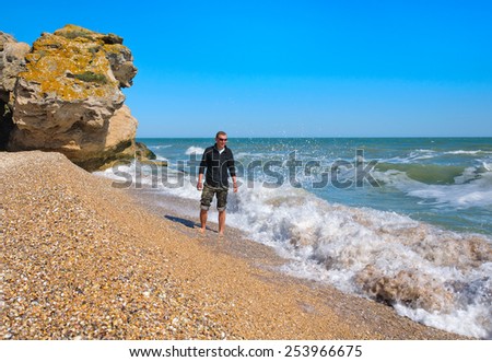 young man stands on the banks of the stormy sea on a sunny day against the blue sky