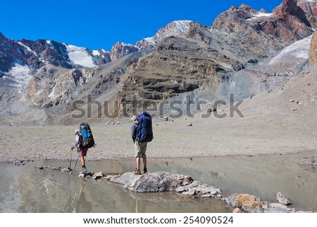 Man with big backpack resting on trekking pole moves a mountain river