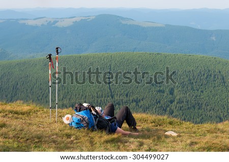Tired hiker relaxes with a large backpack on a slope in the mountains