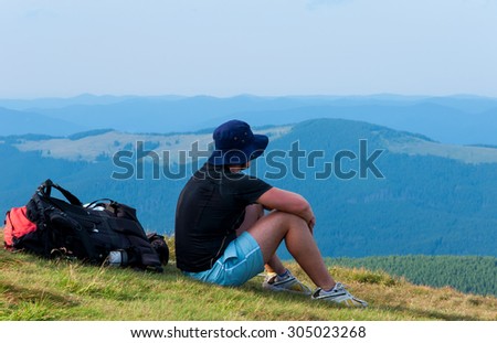 Tired hiker relaxes with a large backpack on a slope in the mountains