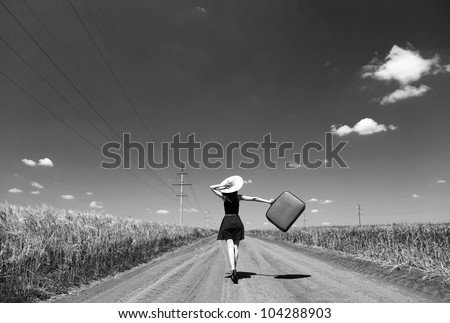 Lonely girl with suitcase at country road. Photo in black and white color style.