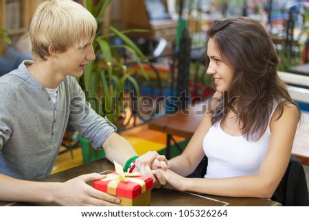 The young man gives a gift to a young girl in the cafe