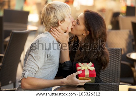 The young man gives a gift to a young girl in the cafe and they are kissing.