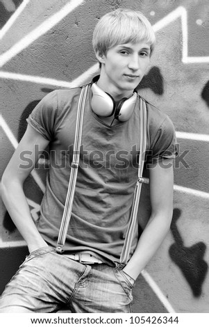 Style teen boy with headphones near graffiti background. Photo in black and white style.