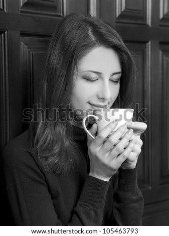 Style girl drinking coffee near wood doors. Photo in black and white style.