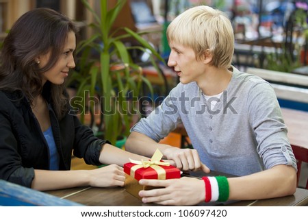 The young man gives a gift to a young girl in the cafe