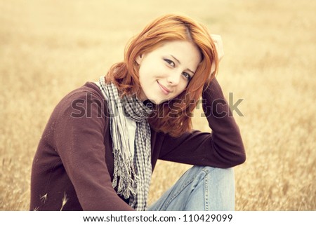 Beautiful red-haired girl at yellow autumn grass.